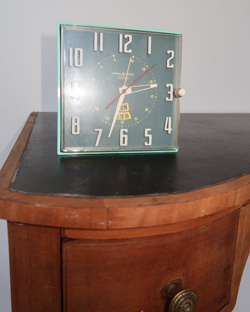 Mid-century turquoise GE Telechron wall clock with white numerals, day-date window, and electric plug-in design.