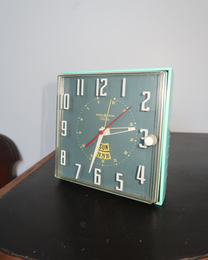 Mid-century turquoise GE Telechron wall clock with white numerals, day-date window, and electric plug-in design.