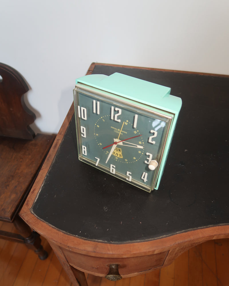 Mid-century turquoise GE Telechron wall clock with white numerals, day-date window, and electric plug-in design.
