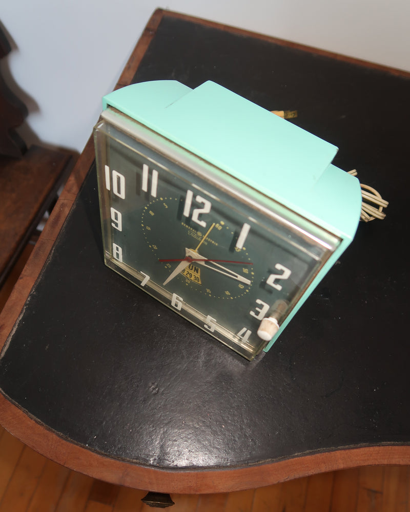 Mid-century turquoise GE Telechron wall clock with white numerals, day-date window, and electric plug-in design.