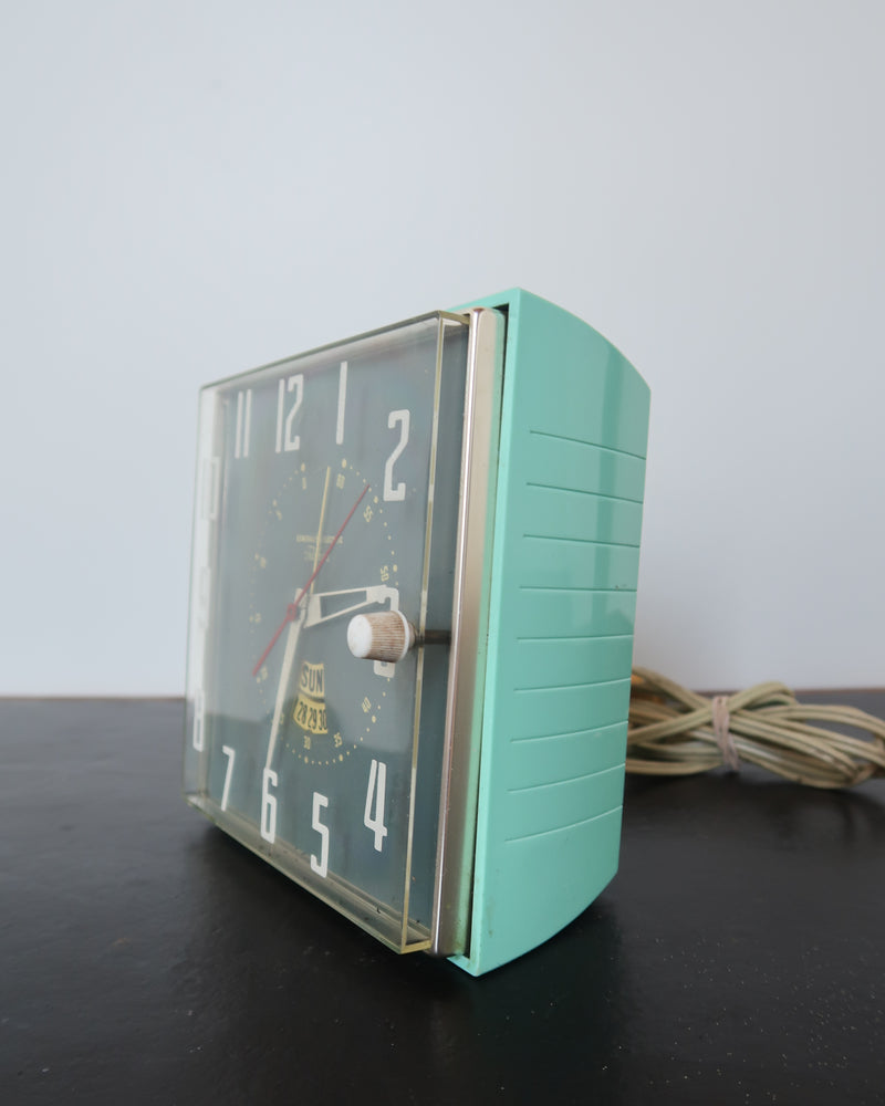 Mid-century turquoise GE Telechron wall clock with white numerals, day-date window, and electric plug-in design.