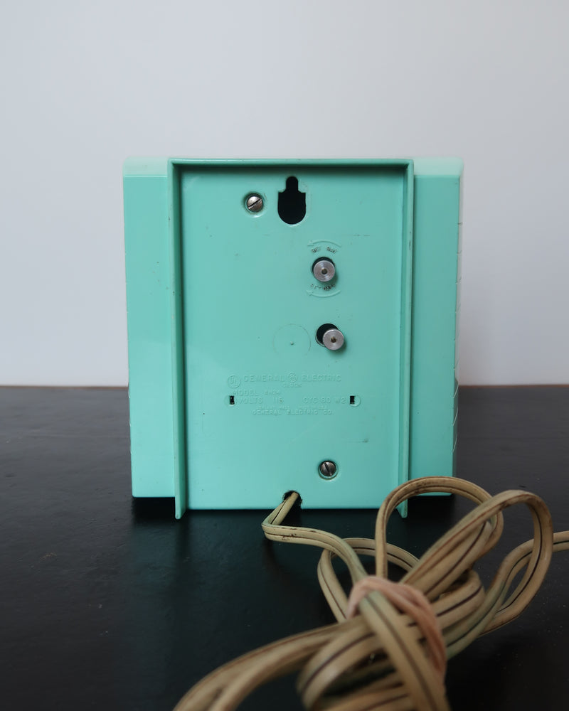 Mid-century turquoise GE Telechron wall clock with white numerals, day-date window, and electric plug-in design.