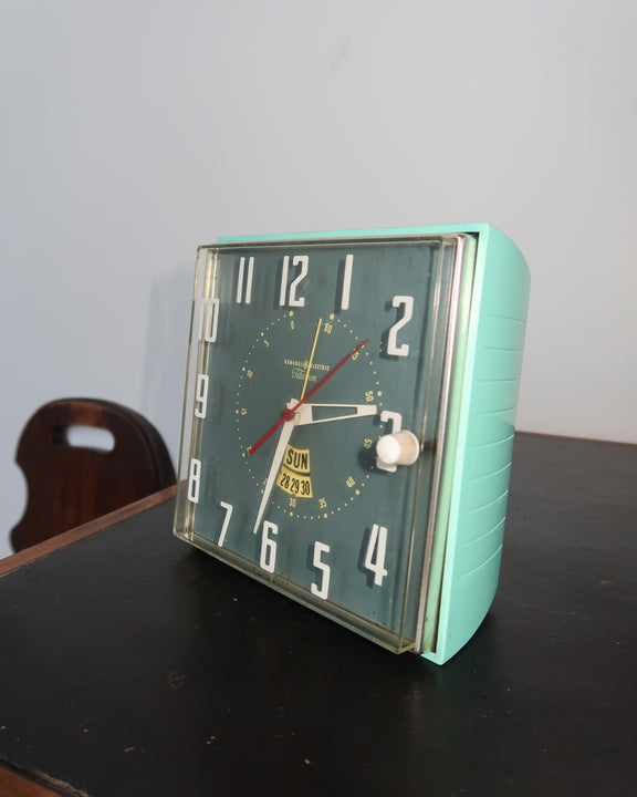Mid-century turquoise GE Telechron wall clock with white numerals, day-date window, and electric plug-in design.