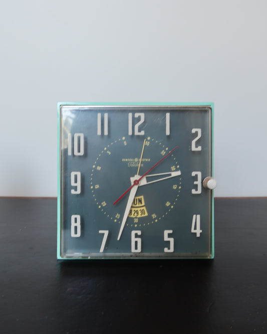 Mid-century turquoise GE Telechron wall clock with white numerals, day-date window, and electric plug-in design.