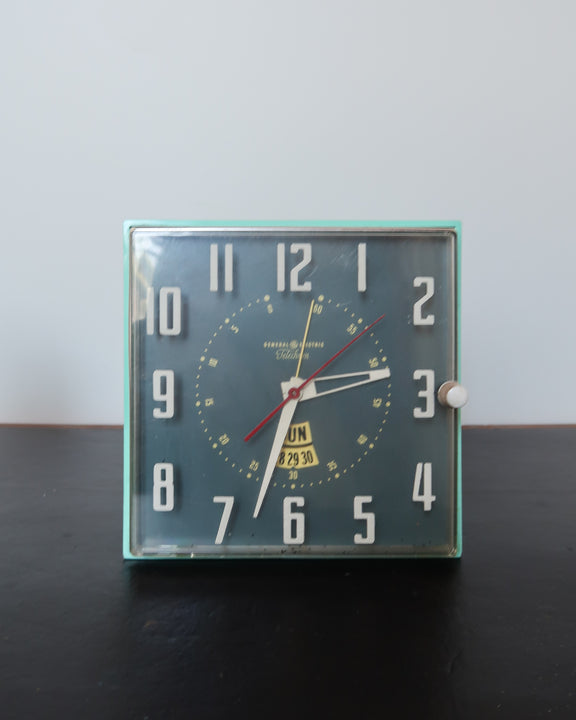 Mid-century turquoise GE Telechron wall clock with white numerals, day-date window, and electric plug-in design.