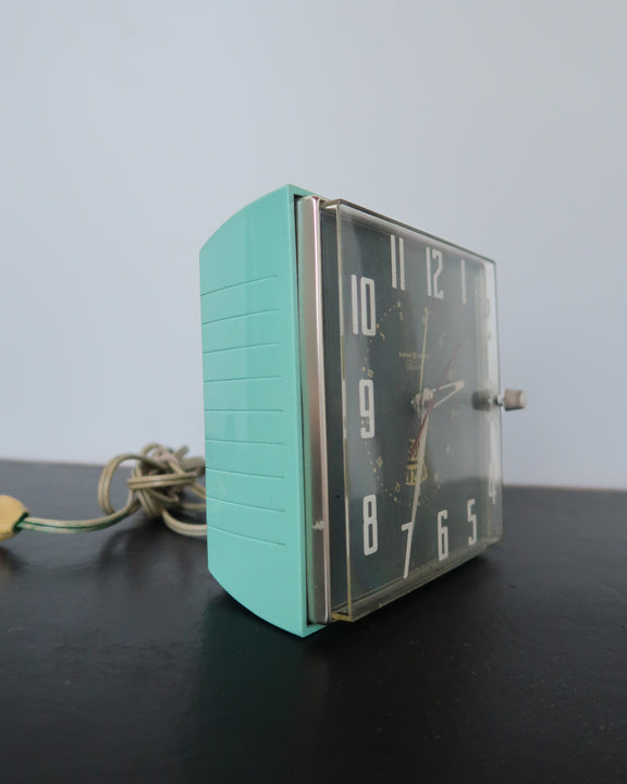 Mid-century turquoise GE Telechron wall clock with white numerals, day-date window, and electric plug-in design.